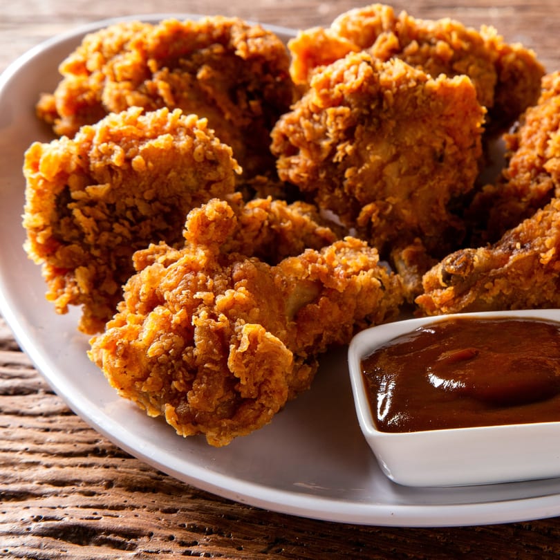 Crispy fried chicken pieces on a white plate with a side of barbecue sauce.