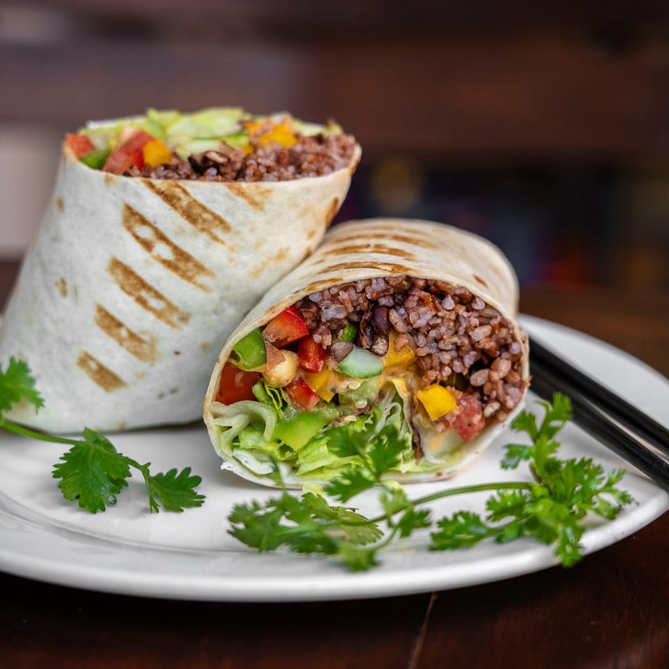 Two deli wraps filled with rice, lettuce, tomatoes, and peppers, garnished with cilantro.
